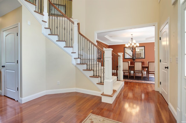 entryway with wood-type flooring, a notable chandelier, a raised ceiling, and ornamental molding