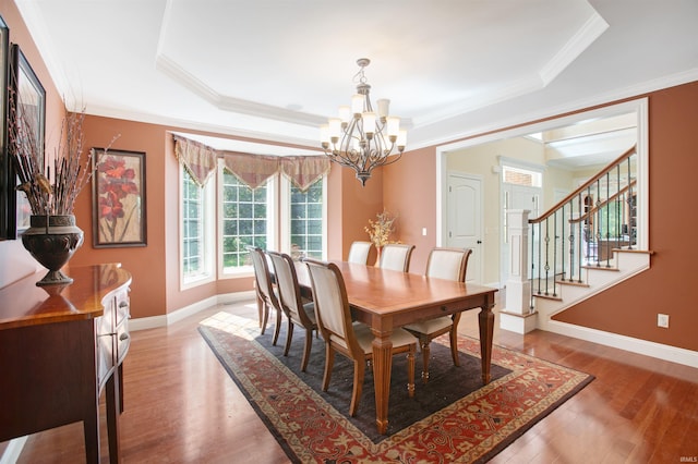 dining room with a raised ceiling, wood-type flooring, ornamental molding, and an inviting chandelier