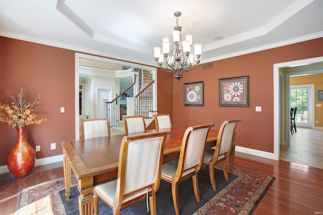 dining room featuring a notable chandelier, a raised ceiling, dark hardwood / wood-style floors, and ornamental molding