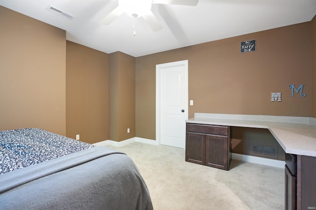 bedroom featuring light colored carpet, ceiling fan, and built in desk