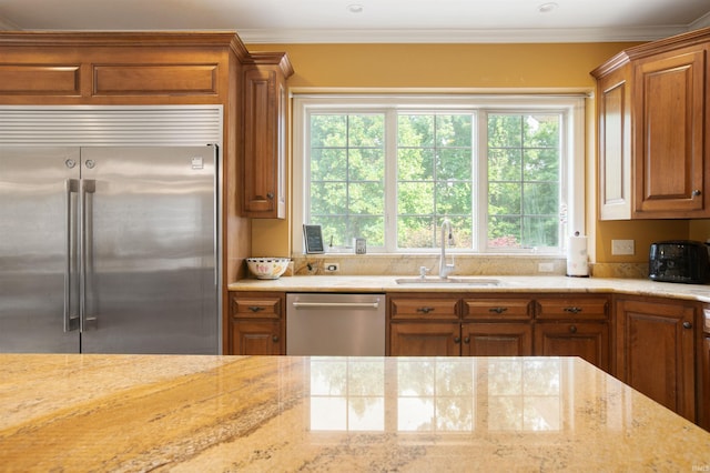 kitchen with appliances with stainless steel finishes, light stone counters, crown molding, and sink