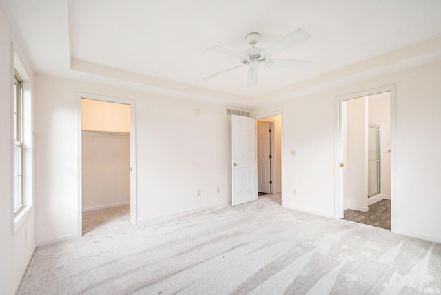 unfurnished bedroom featuring a closet, ceiling fan, light carpet, and a walk in closet