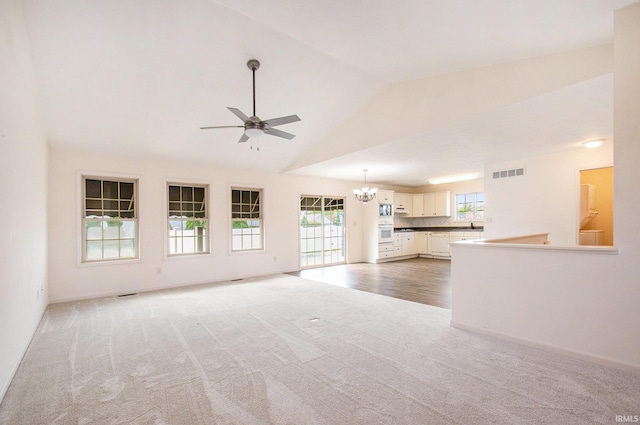 unfurnished living room with light colored carpet, high vaulted ceiling, and ceiling fan with notable chandelier