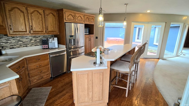 kitchen featuring a center island, dark wood-type flooring, appliances with stainless steel finishes, decorative light fixtures, and backsplash