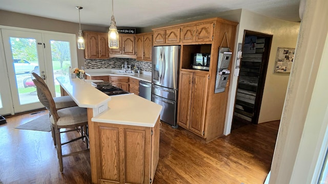 kitchen featuring decorative backsplash, hardwood / wood-style floors, a breakfast bar area, appliances with stainless steel finishes, and decorative light fixtures