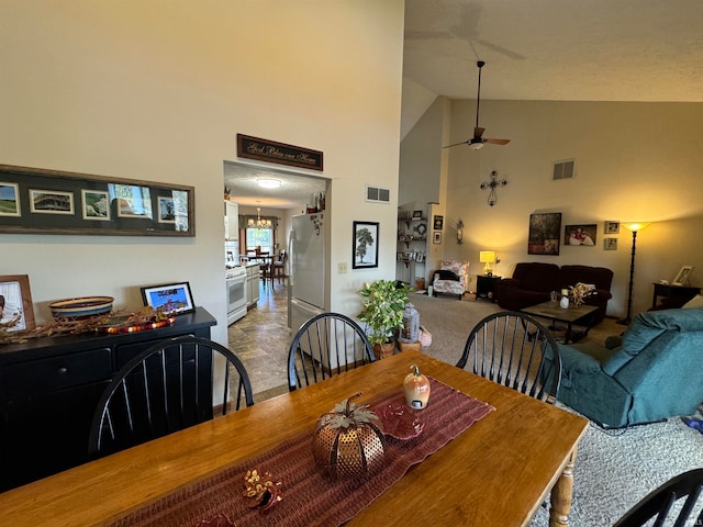 dining space with ceiling fan with notable chandelier and high vaulted ceiling