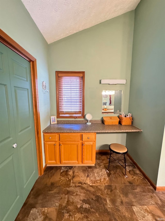 home office featuring a textured ceiling, built in desk, and vaulted ceiling