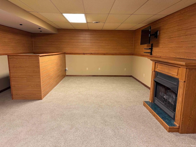 basement featuring wood walls, a drop ceiling, and light carpet