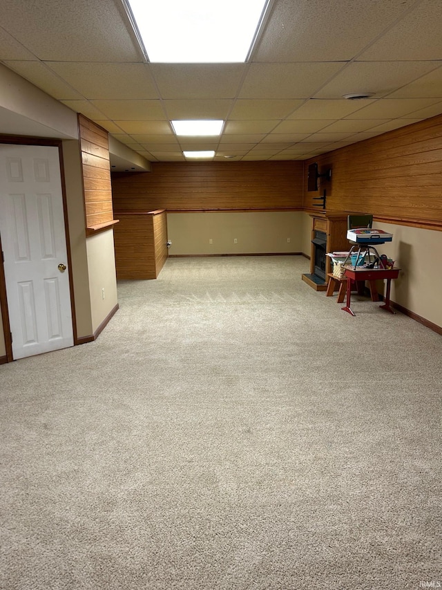 basement featuring wood walls, a drop ceiling, and light carpet