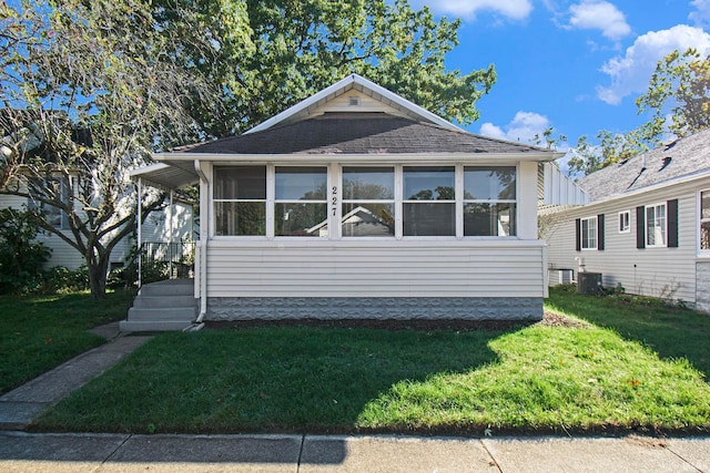 view of front of house with a sunroom, a front lawn, and central air condition unit