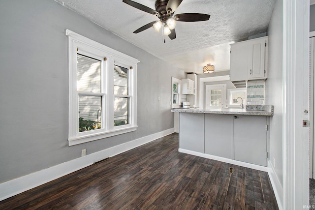 kitchen featuring sink, kitchen peninsula, a textured ceiling, dark wood-type flooring, and white cabinetry