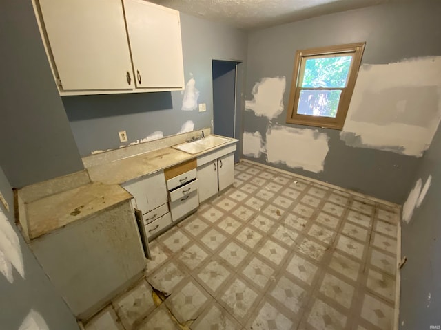 kitchen with sink, a textured ceiling, and white cabinetry