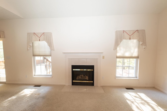 unfurnished living room featuring light colored carpet, a tiled fireplace, and a healthy amount of sunlight