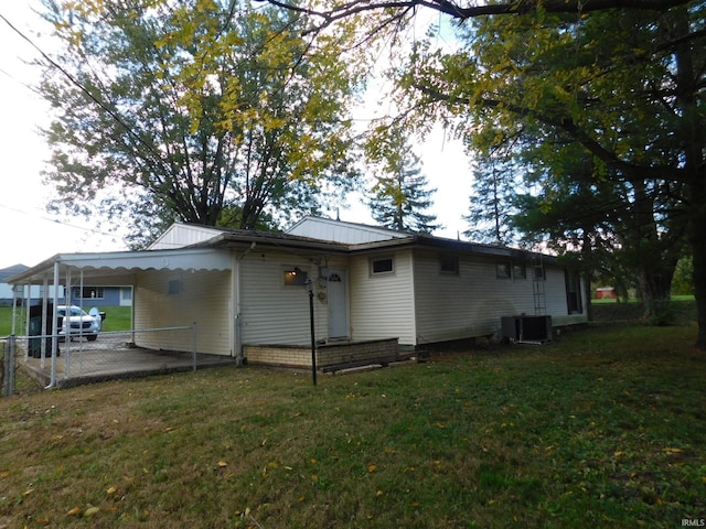 back of house featuring cooling unit, a carport, and a lawn