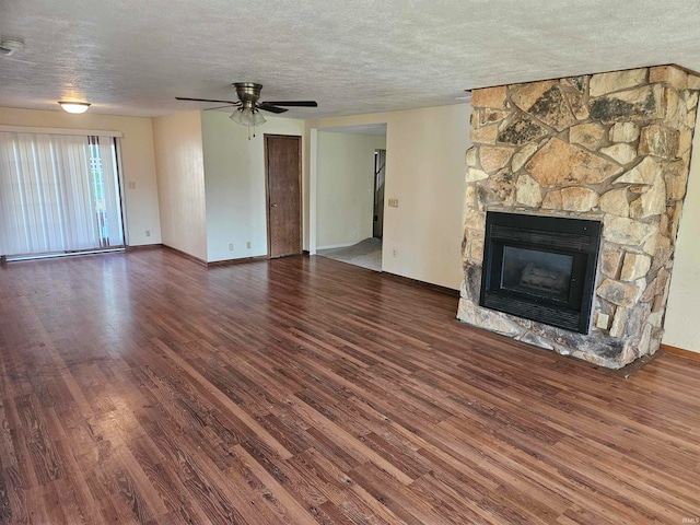 unfurnished living room with ceiling fan, dark hardwood / wood-style floors, a stone fireplace, and a textured ceiling