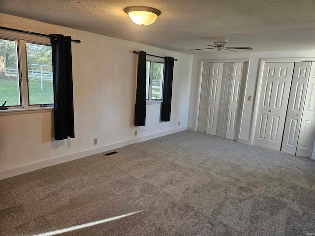 unfurnished bedroom featuring ceiling fan, carpet floors, and two closets