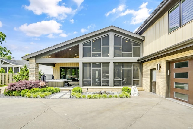 back of property featuring a sunroom, a patio, and a hot tub