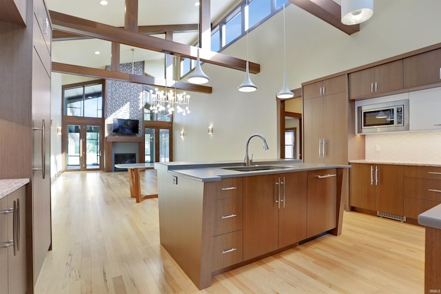 kitchen featuring sink, stainless steel microwave, a fireplace, light hardwood / wood-style flooring, and decorative light fixtures