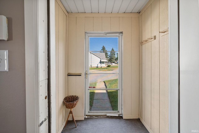 doorway with wood walls, wood ceiling, and dark colored carpet