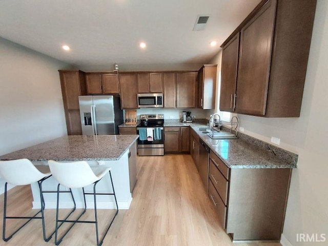 kitchen featuring dark stone counters, light hardwood / wood-style flooring, sink, stainless steel appliances, and a center island