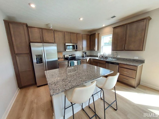 kitchen with a kitchen island, light stone countertops, light hardwood / wood-style flooring, appliances with stainless steel finishes, and a kitchen bar