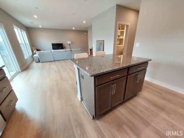 kitchen featuring dark brown cabinets, a kitchen island, light hardwood / wood-style flooring, and stone countertops