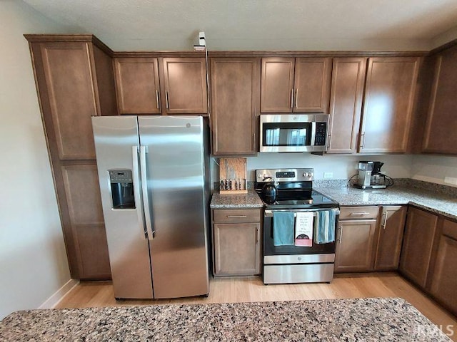 kitchen featuring light stone counters, appliances with stainless steel finishes, and light hardwood / wood-style flooring