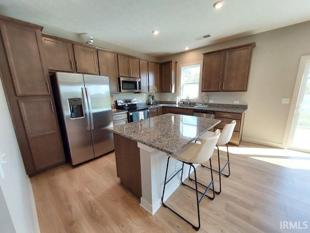 kitchen with light wood-type flooring, a kitchen breakfast bar, stainless steel appliances, light stone countertops, and a center island