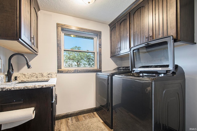 laundry area with cabinets, a textured ceiling, washer and dryer, light wood-type flooring, and sink