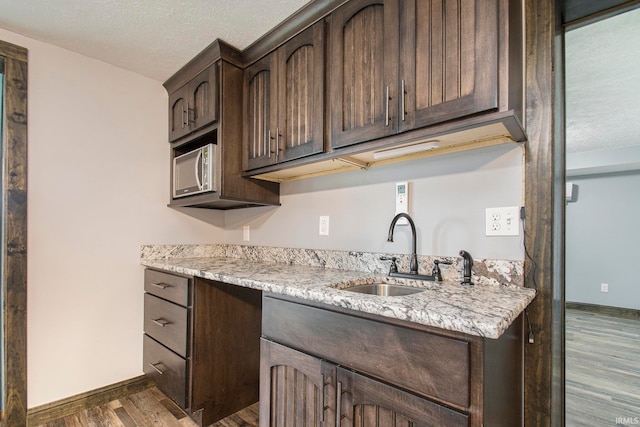 kitchen featuring dark brown cabinets, a textured ceiling, light stone countertops, dark wood-type flooring, and sink