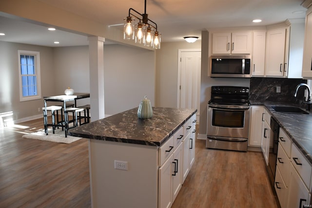 kitchen featuring hanging light fixtures, white cabinetry, wood-type flooring, stainless steel appliances, and sink