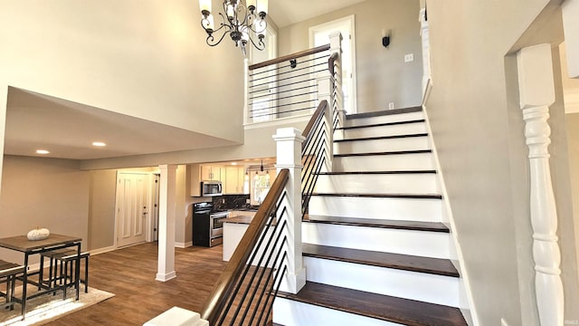 staircase with decorative columns, a notable chandelier, a towering ceiling, and hardwood / wood-style floors