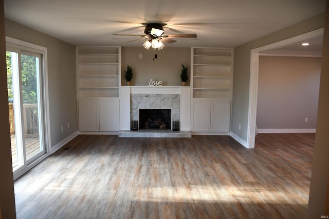 unfurnished living room with ceiling fan, built in features, wood-type flooring, and a tile fireplace