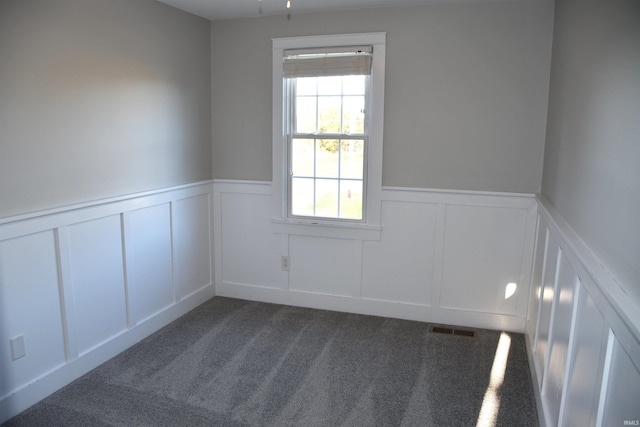 empty room with visible vents, a wainscoted wall, dark colored carpet, and a decorative wall