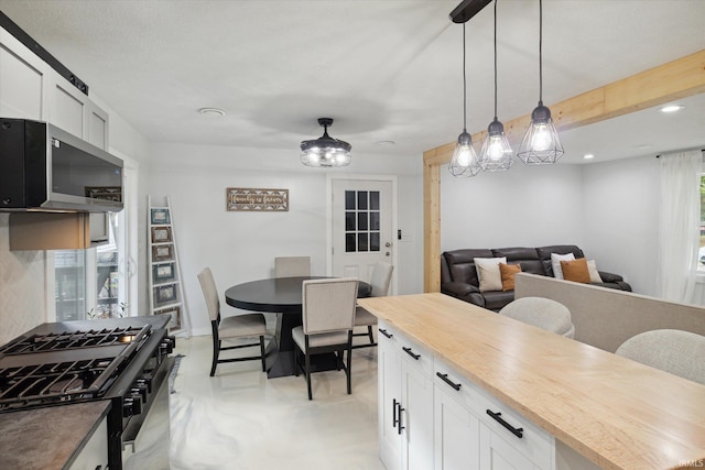 kitchen featuring butcher block countertops, appliances with stainless steel finishes, hanging light fixtures, and white cabinets