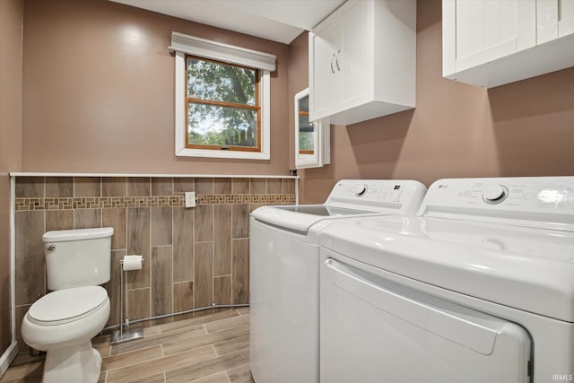 clothes washing area with washing machine and dryer, light wood-type flooring, and tile walls