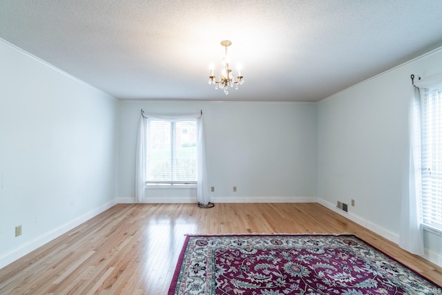 empty room with a notable chandelier, a healthy amount of sunlight, and light wood-type flooring