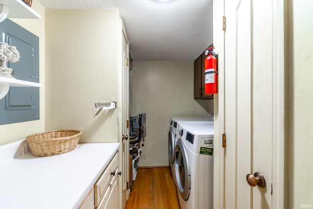 laundry area featuring washing machine and clothes dryer, cabinets, electric panel, a textured ceiling, and light hardwood / wood-style floors