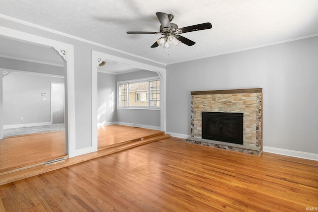 unfurnished living room featuring ornamental molding, a stone fireplace, wood-type flooring, and ceiling fan