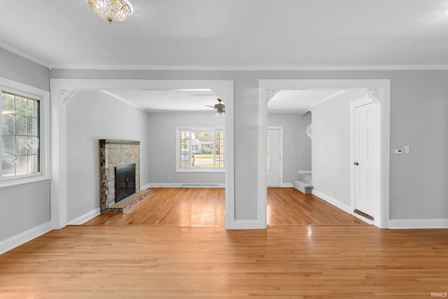 unfurnished living room with a stone fireplace, ceiling fan, light wood-type flooring, and a wealth of natural light