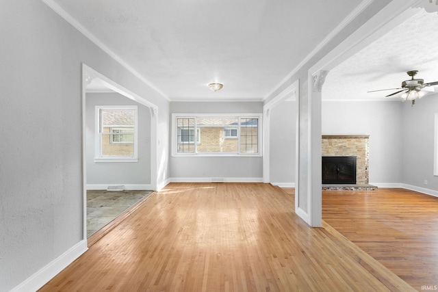 unfurnished living room featuring crown molding, light hardwood / wood-style flooring, a stone fireplace, and ceiling fan