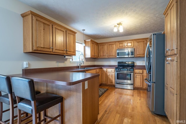 kitchen with appliances with stainless steel finishes, dark countertops, brown cabinets, a sink, and a peninsula