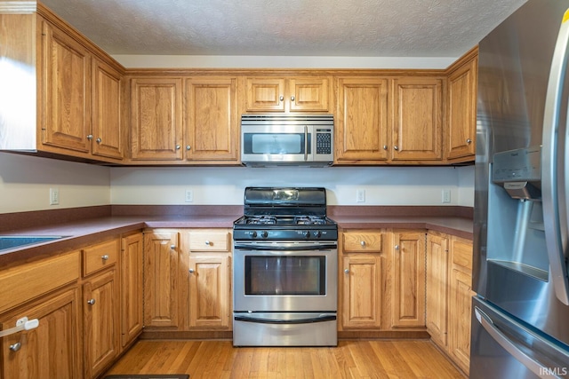 kitchen with dark countertops, appliances with stainless steel finishes, brown cabinetry, and light wood-style floors