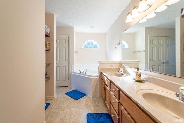 bathroom featuring vanity, a relaxing tiled tub, a textured ceiling, and tile patterned flooring