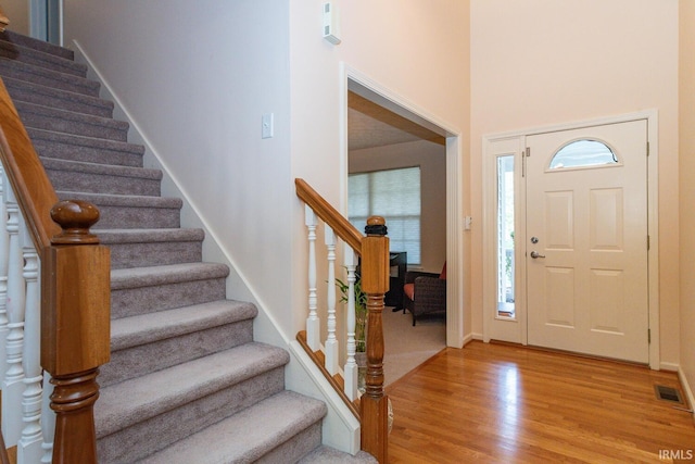 entrance foyer with a high ceiling, baseboards, light wood-type flooring, visible vents, and stairway
