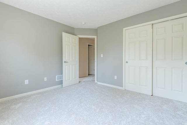 unfurnished bedroom featuring baseboards, light carpet, a closet, and visible vents