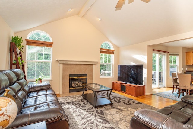 living room featuring beam ceiling, a tiled fireplace, ceiling fan, high vaulted ceiling, and light wood-type flooring