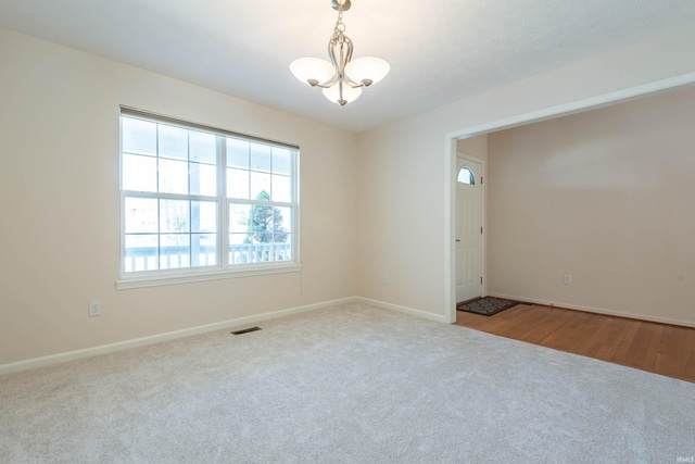 carpeted spare room with baseboards, an inviting chandelier, and visible vents