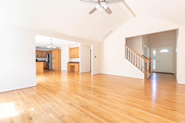 unfurnished living room featuring light wood-type flooring, lofted ceiling with beams, stairs, and ceiling fan with notable chandelier