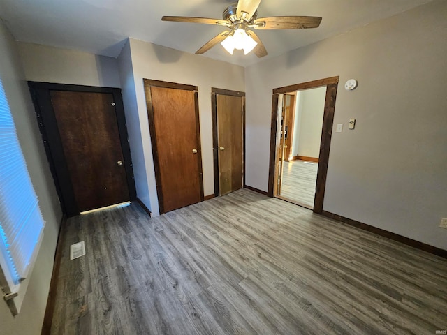 unfurnished bedroom with multiple closets, ceiling fan, and wood-type flooring